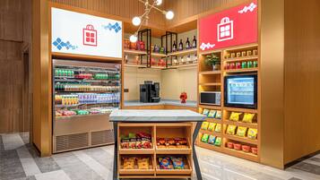 Ein gut beleuchteter Imbissstand mit Regalen voller Snacks und Getränke, einer Kaffeemaschine und einem digitalen Bildschirm.