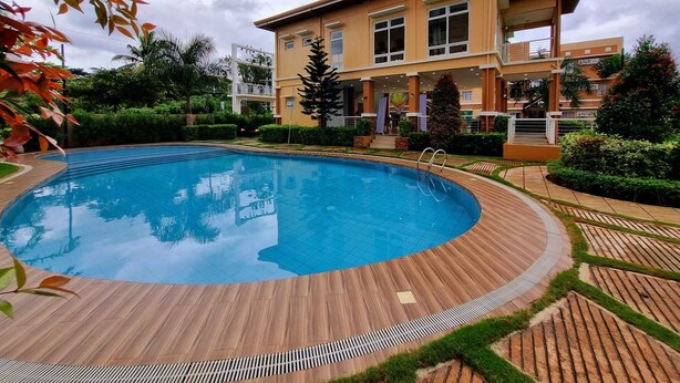Un hotel moderno con piscina, rodeado de jardines cuidados y un edificio de varios pisos con balcones.