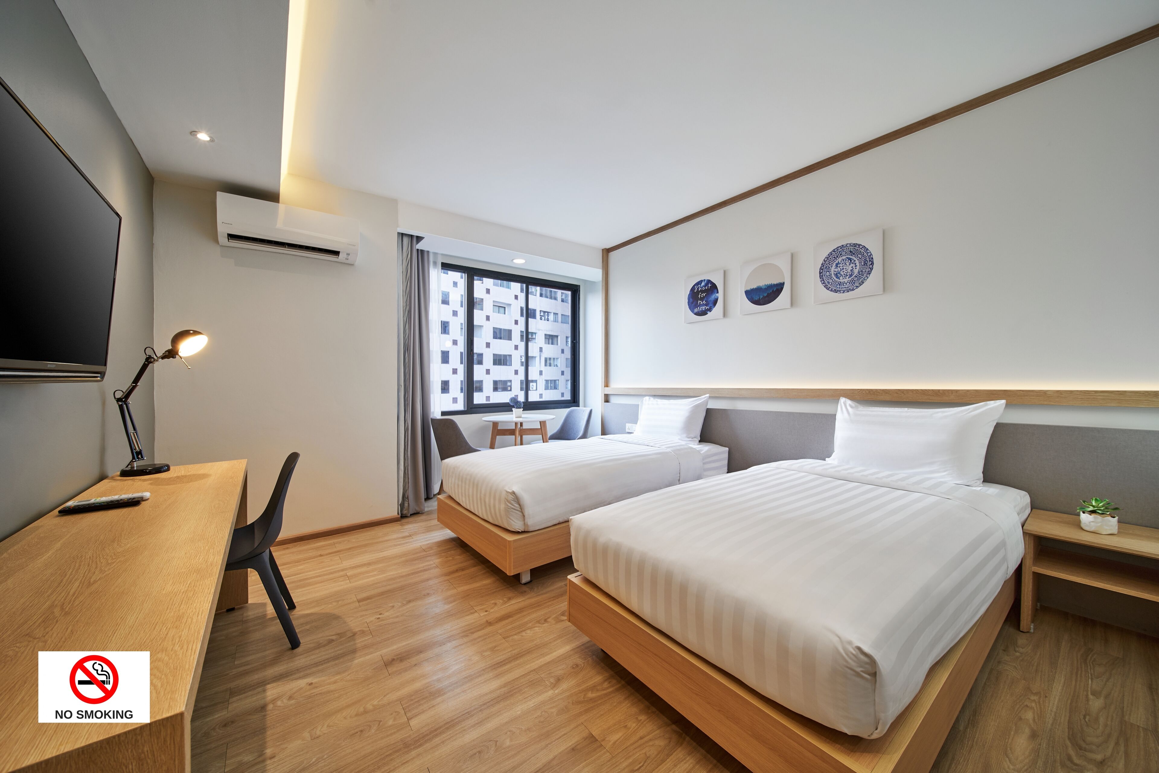 A modern hotel room with two beds, a desk, a TV, and a window with a city view.