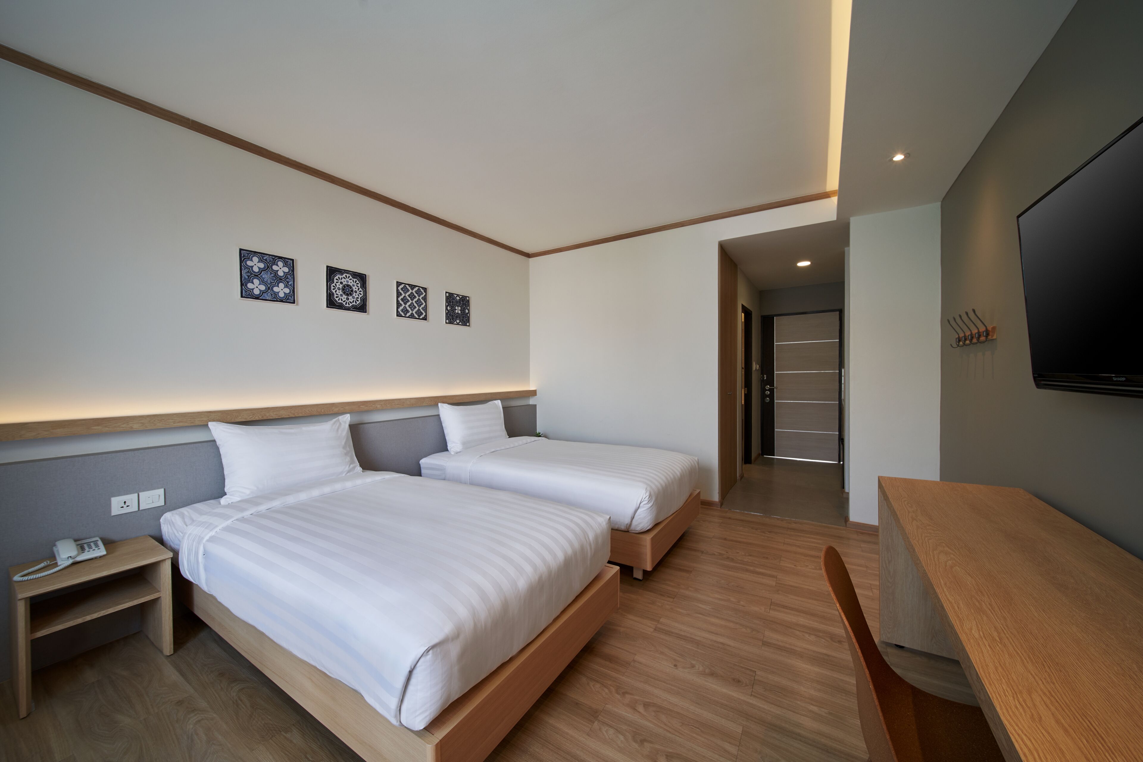 Et moderne hotelværelse med to senge, et trænatbord, et skrivebord og et fjernsyn.