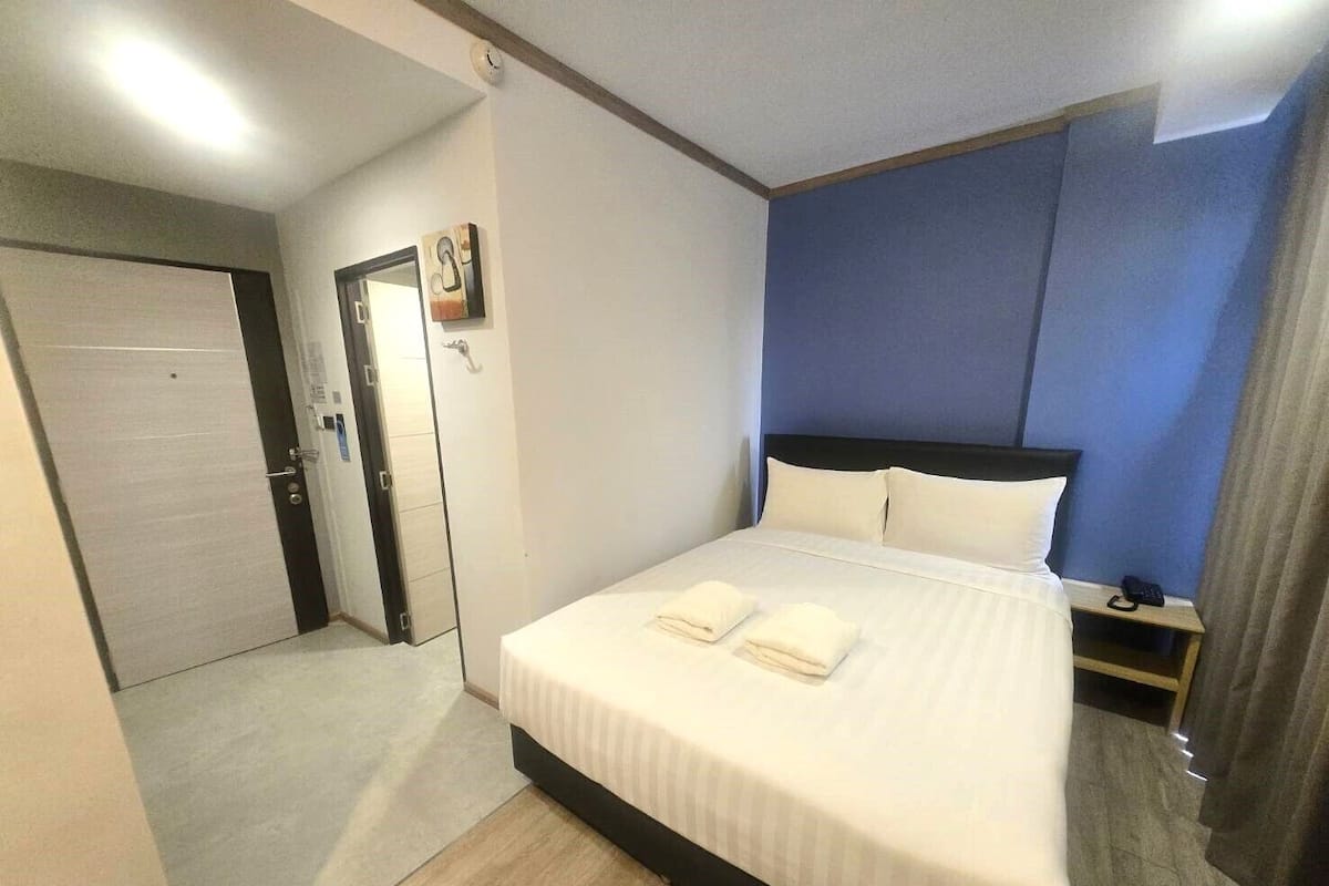 Une chambre d’hôtel avec un lit, une table de chevet, une porte et un mur agrémenté d’une touche de bleu.