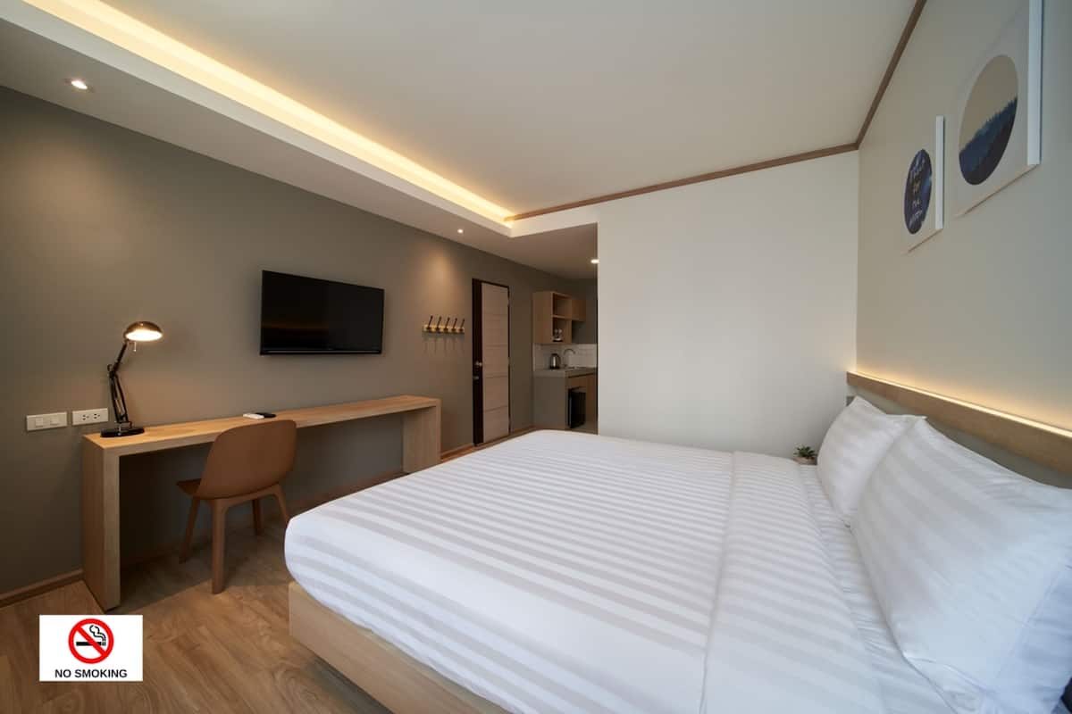 Une chambre d’hôtel moderne équipée d’un lit, d’un bureau, d’une chaise et d’un téléviseur fixé au mur.