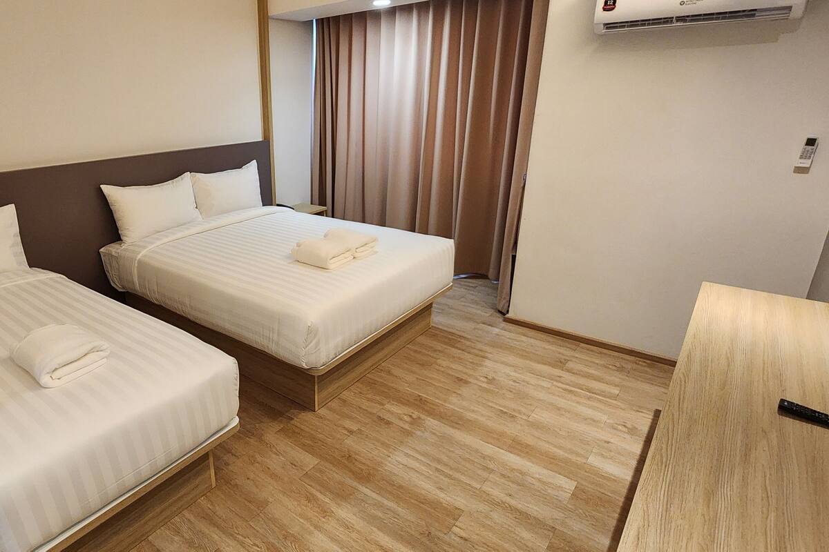 Une chambre d’hôtel avec deux lits simples, un plancher en bois, un bureau et un appareil de climatisation.