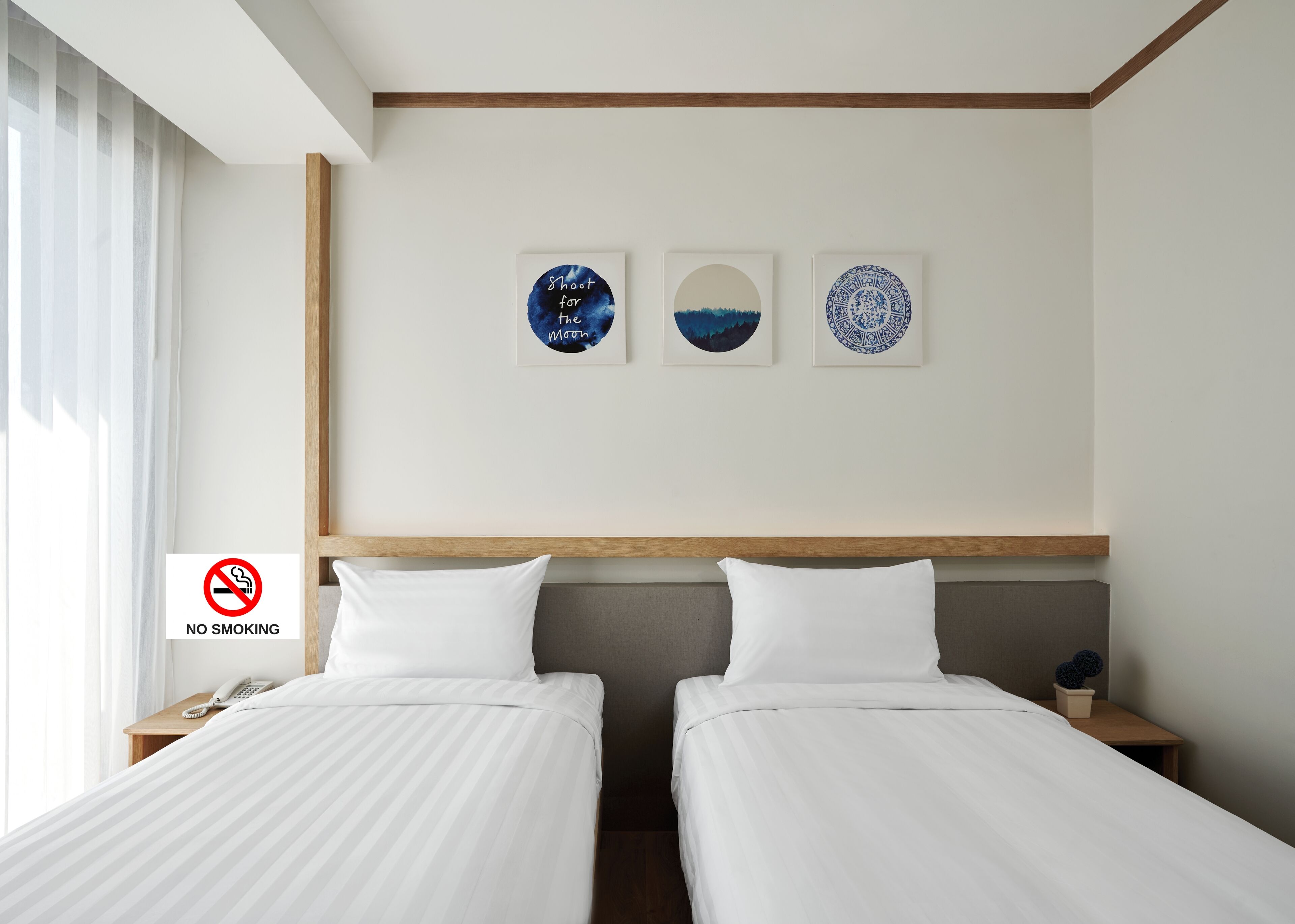 A hotel room with two beds, a wooden headboard, and three wall art pieces.