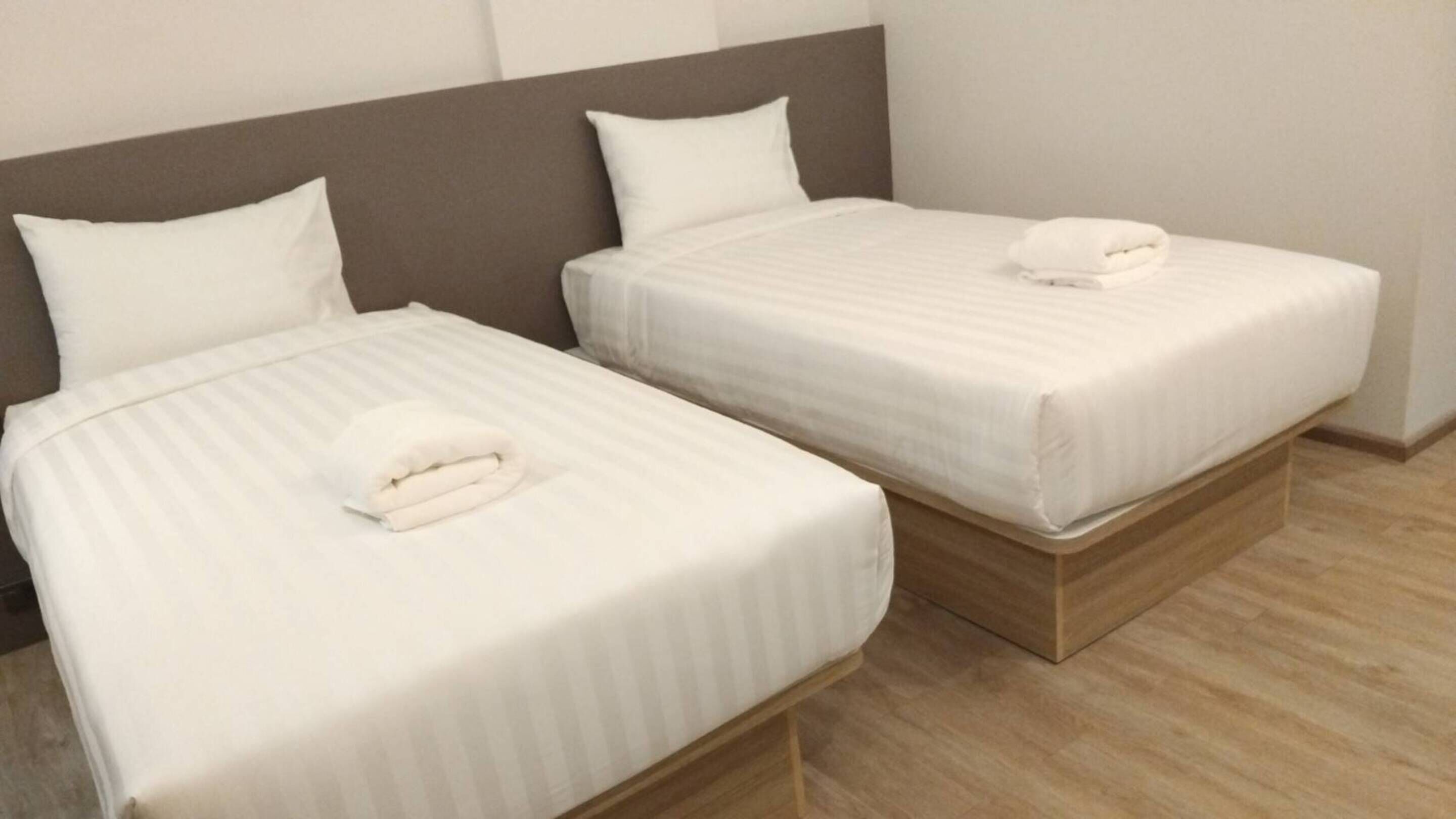 Two single beds with white linens and pillows, a wooden headboard, and a light-colored wooden floor.