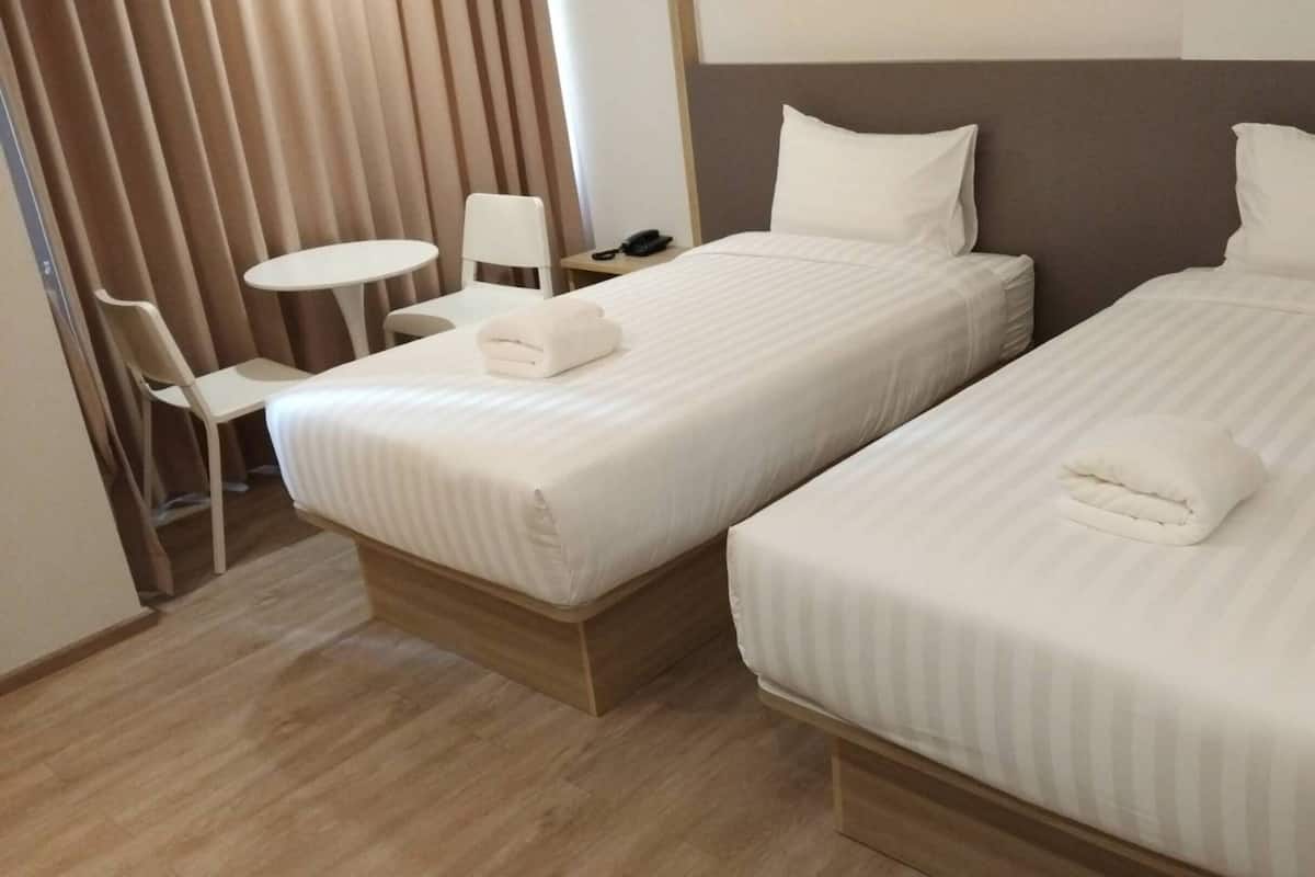Une chambre d’hôtel avec deux lits, une petite table, une chaise et un rideau.
