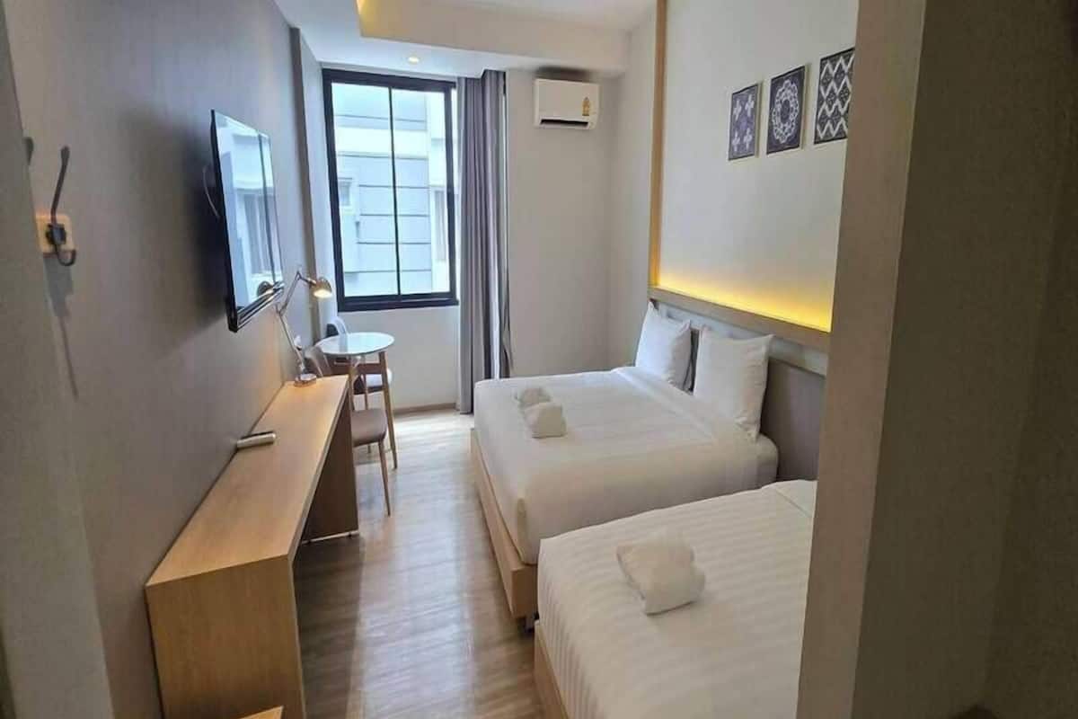 Une chambre d’hôtel avec deux lits, un bureau, une chaise, une télévision et une fenêtre avec des rideaux.
