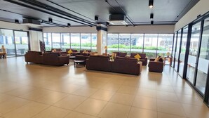 A spacious lobby with multiple sofas and a coffee table, large windows offering a view of the outdoors, and a modern industrial ceiling design. - Prom Thailand Cultural Centre Hotel Annex2 (Bangkok)