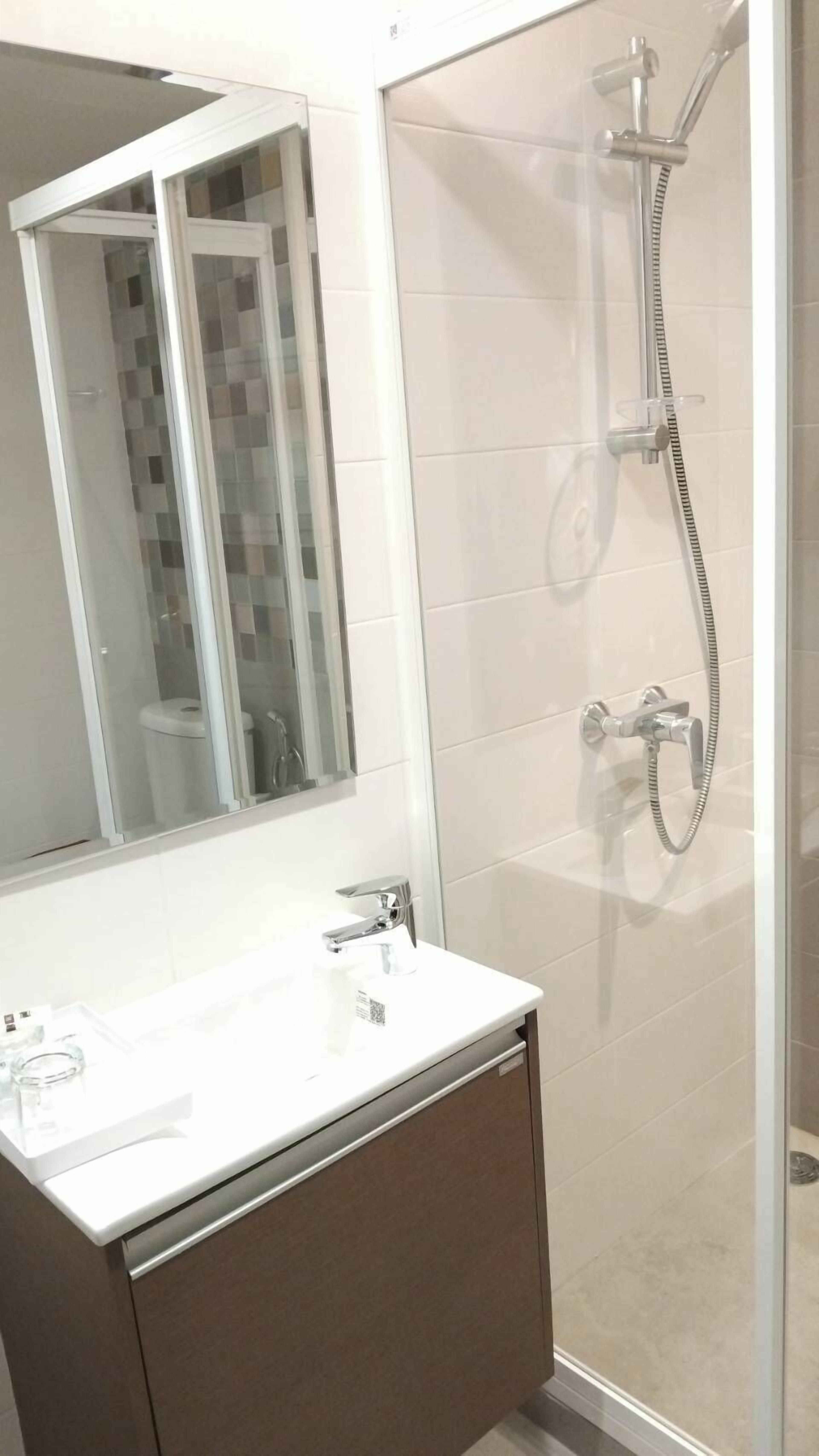 Un baño moderno con cabina de ducha de vidrio, un lavabo blanco y un espejo grande.
