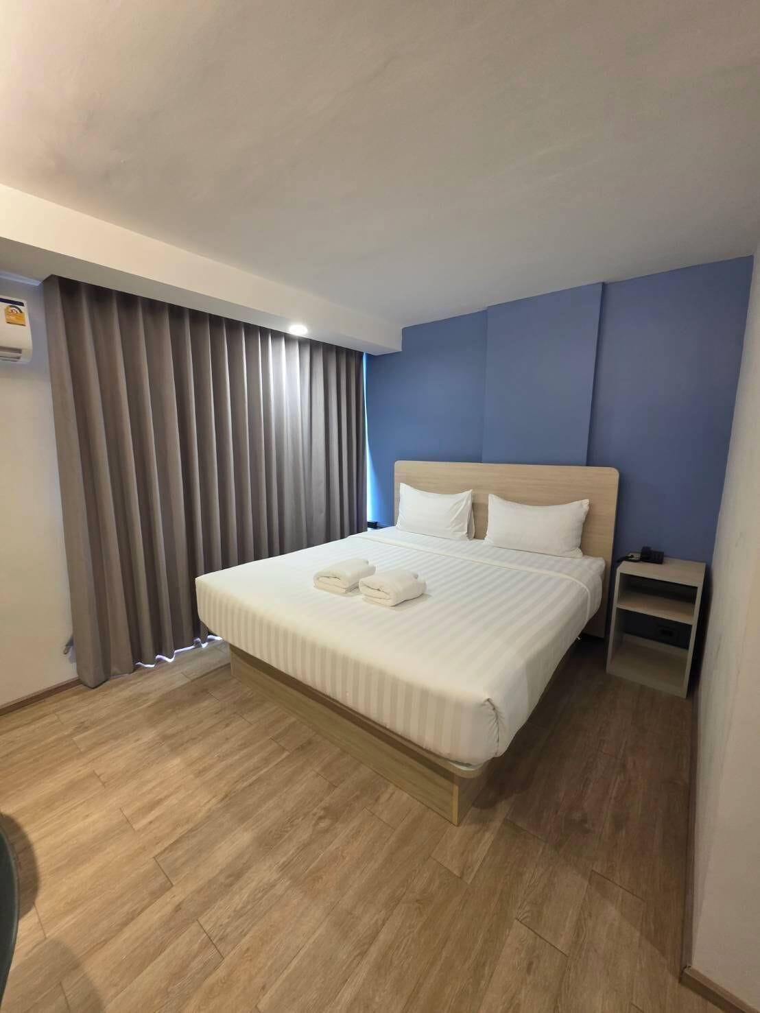A hotel room with a large bed, a nightstand, and a window with curtains.