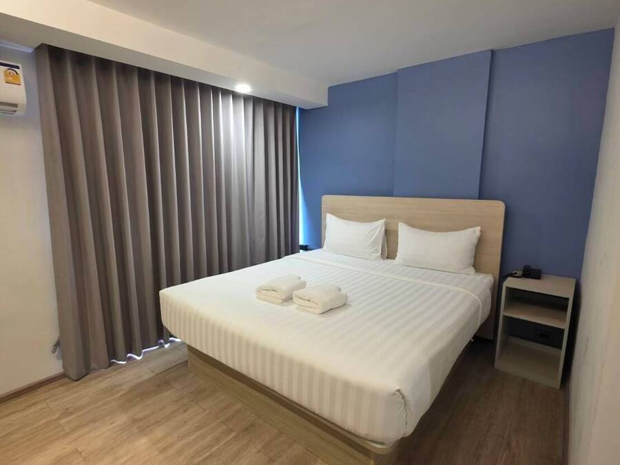 A hotel room with a large bed, a nightstand, and a window with curtains.