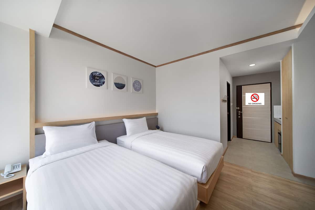 Une chambre d’hôtel avec deux lits, un téléphone sur la table de chevet et un panneau « Interdiction de fumer » sur la porte.