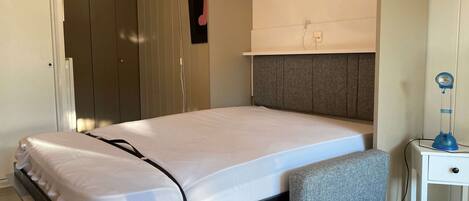A neatly made bed with a grey headboard, a bedside table with a lamp, and a chair.