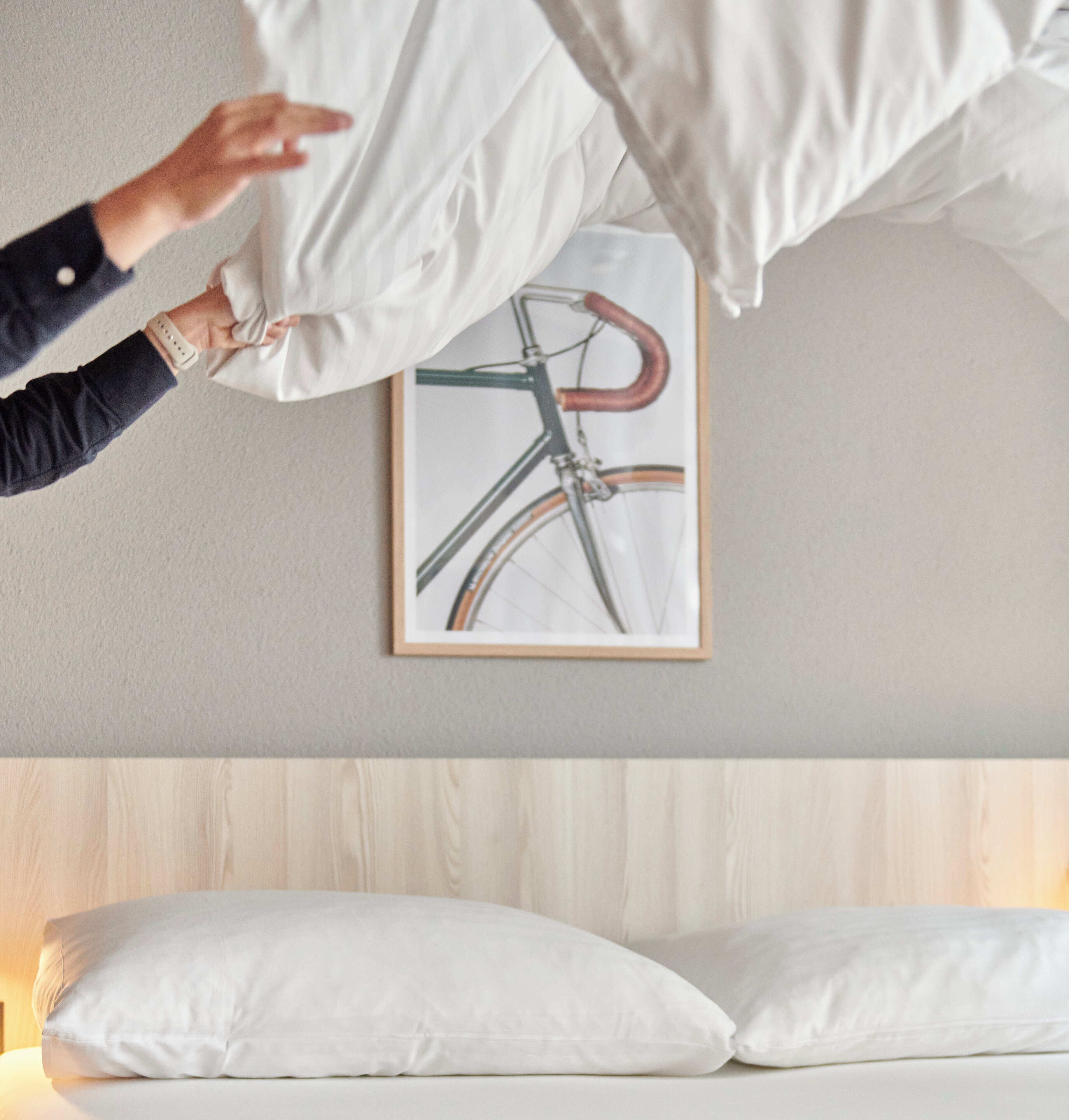 A bedroom with a bed, pillows, a framed picture of a bicycle on the wall, and a wooden headboard.