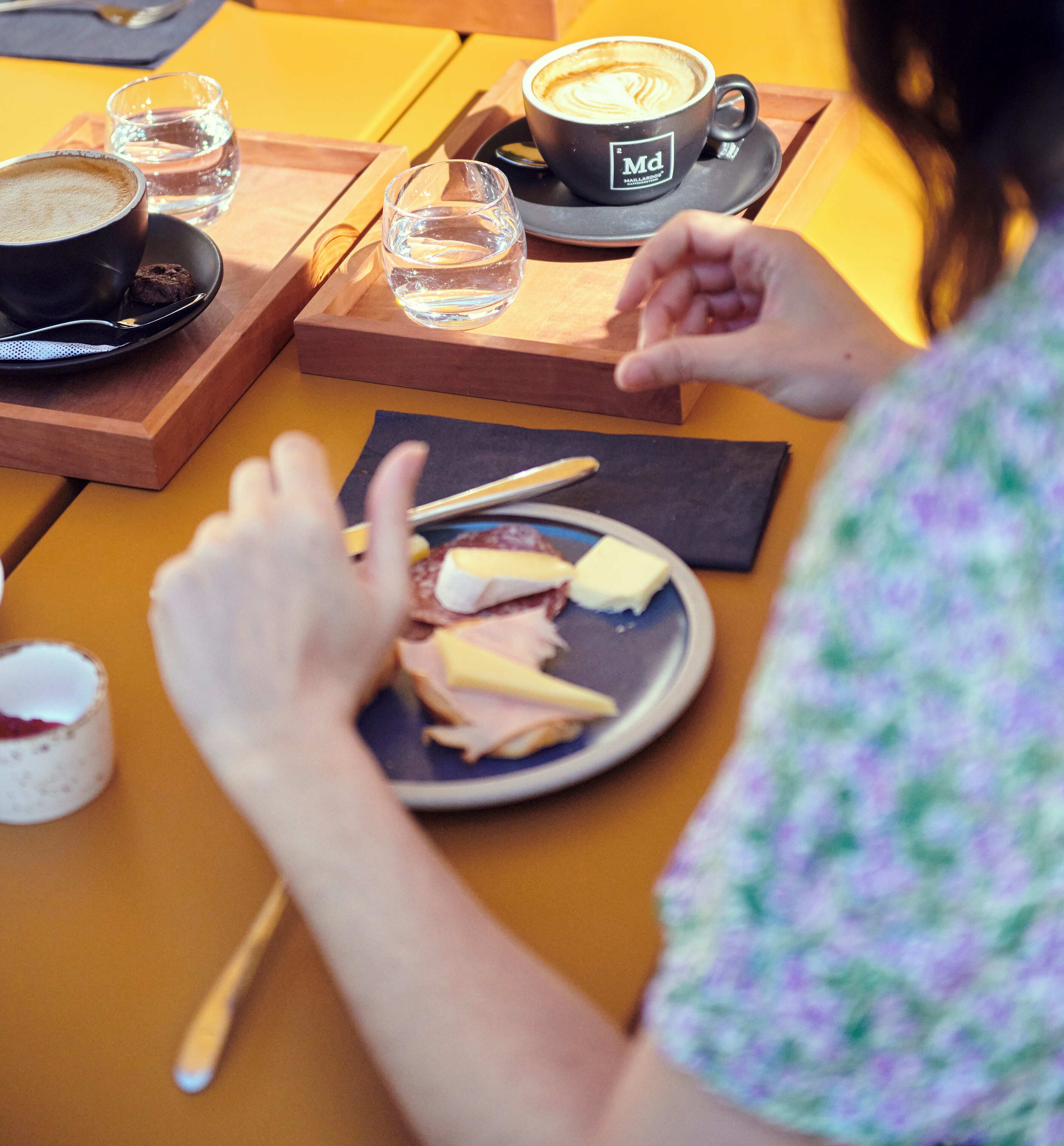 A person sitting at a wooden table with a plate of food, a cup of coffee, and a glass of water.