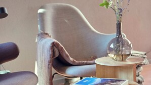 A modern living room with a curved armchair, a round wooden side table with a book, and a vase with flowers. - Hotel Balga Natur- und Bikehotel (Balgach)