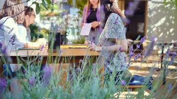 A group of people gathered around a table in an outdoor setting with plants and flowers.