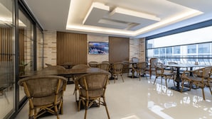 A modern dining area with wicker chairs and tables, a large TV screen, and a view of the city through large windows. - Rubby Kadıköy (Istanbul)