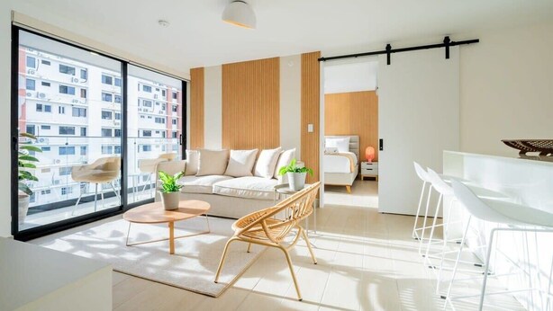 A modern living room with a sofa, coffee table, and chairs, large windows with a city view, and a sliding door leading to another room. - w* | Roomy 1BR in San Francisco w/ Pool (Panamá)