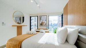 A modern hotel room with a large bed, a wooden headboard, a round mirror, a desk, and a view of the city through large windows. - w* | Roomy 1BR in San Francisco w/ Pool (Panamá)