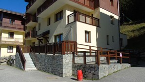 A multi-story building with balconies, a stone wall, and a red barrel.
