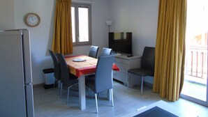 A compact living space with a dining area, a TV, and a window with curtains.