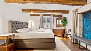 A bedroom with a large bed, wooden beams, a window, a dresser, a bench, and a mirror. - Charming Grund Retreat Near Neumünster Abbey (Luxembourg)