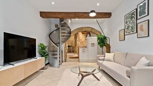 A modern living room with a flat-screen TV, a sofa, a glass coffee table, and a spiral staircase leading to an open kitchen area. - Charming Grund Retreat Near Neumünster Abbey (Luxembourg)