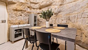 A dining area with a stone wall backdrop, a table with woven placemats, black chairs, and a white vase with greenery. - Charming Grund Retreat Near Neumünster Abbey (Luxembourg)