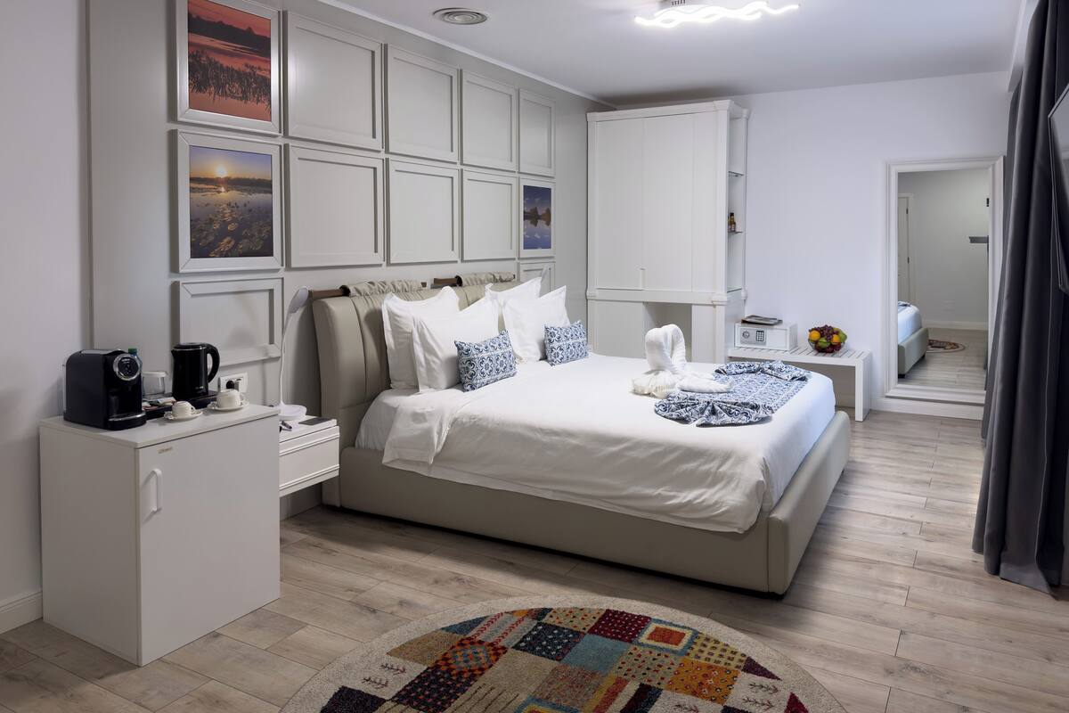 A modern hotel room with a large bed, a small desk, a coffee maker, and a fruit bowl.
