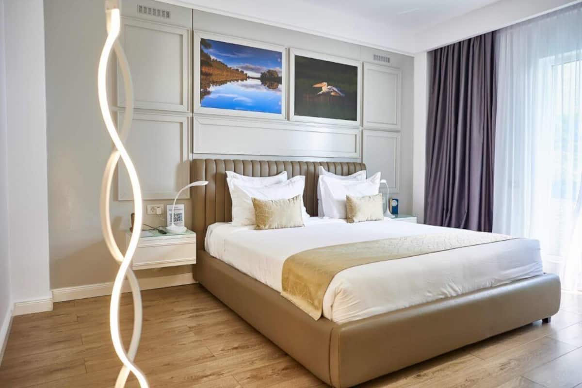 A modern hotel room with a large bed, a nightstand, and two framed pictures on the wall.