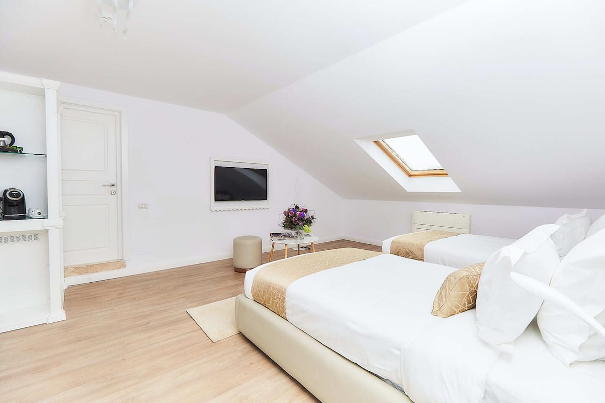 A modern bedroom with a skylight, a bed, a bedside table, and a small side table with a vase of flowers.