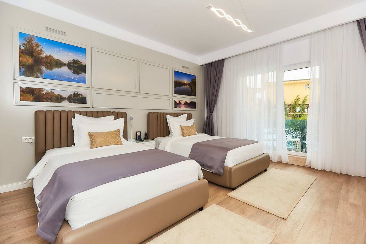 A hotel room with two beds, a large window with curtains, and wall-mounted artwork.