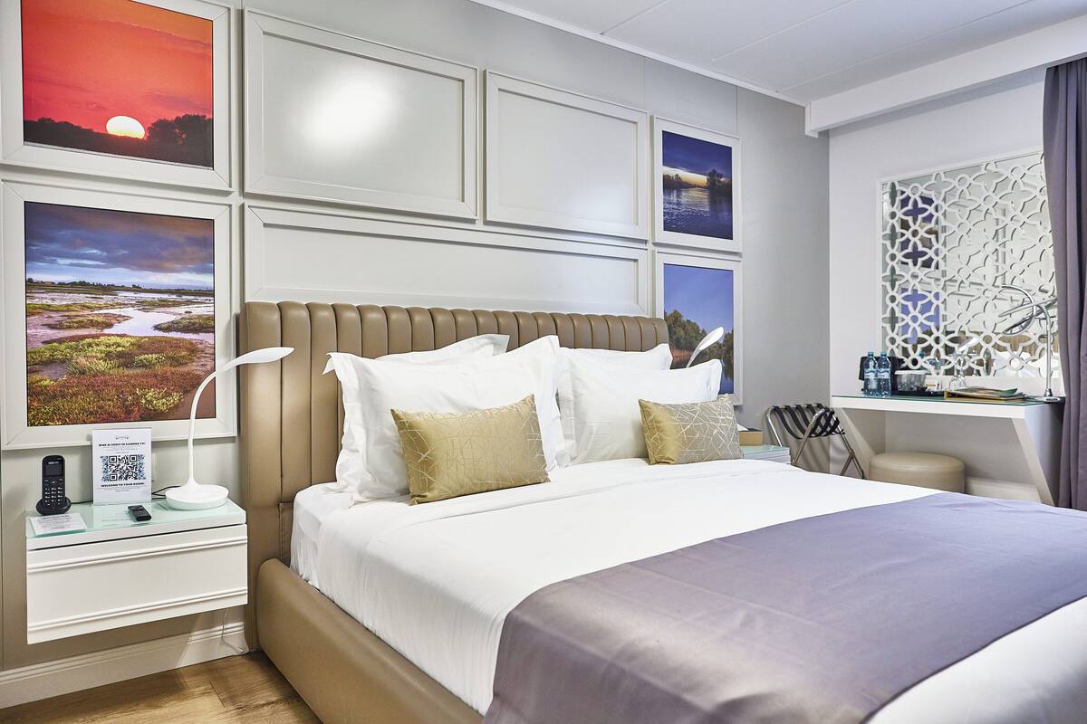 A neatly arranged hotel room with a large bed, a bedside table with a lamp, and artwork on the walls.