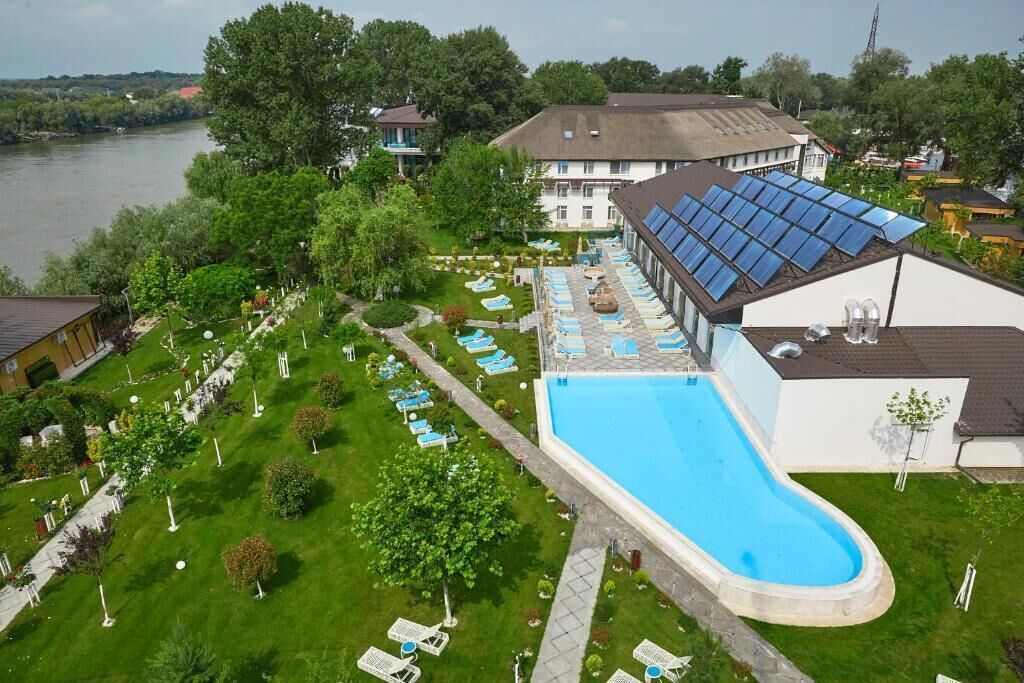 A swimming pool with sun loungers, a covered area with solar panels, and a view of a river.