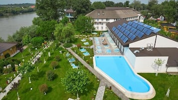 A swimming pool with sun loungers, a covered area with solar panels, and a view of a river.
