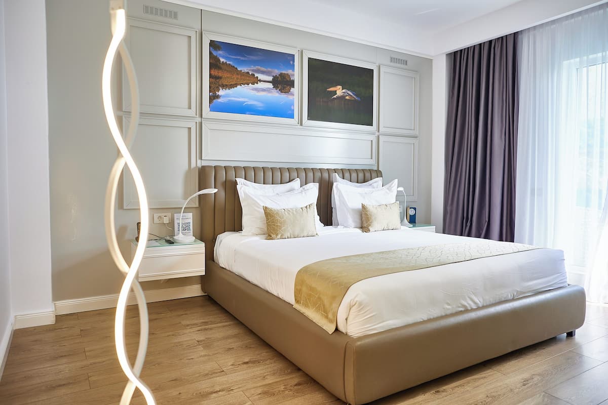 A modern hotel room with a large bed, two bedside tables, and artwork on the wall.