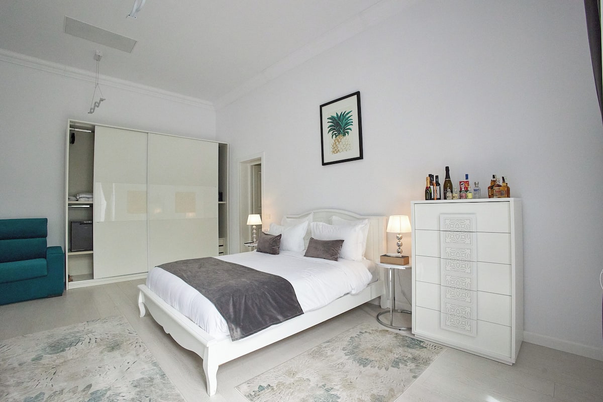 A bedroom with a bed, a wardrobe, a nightstand, and a teal chair.