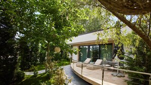 A modern outdoor deck with lounge chairs and a dining area, surrounded by lush greenery and trees. - Lebada Luxury Resort & Spa (Crisan)