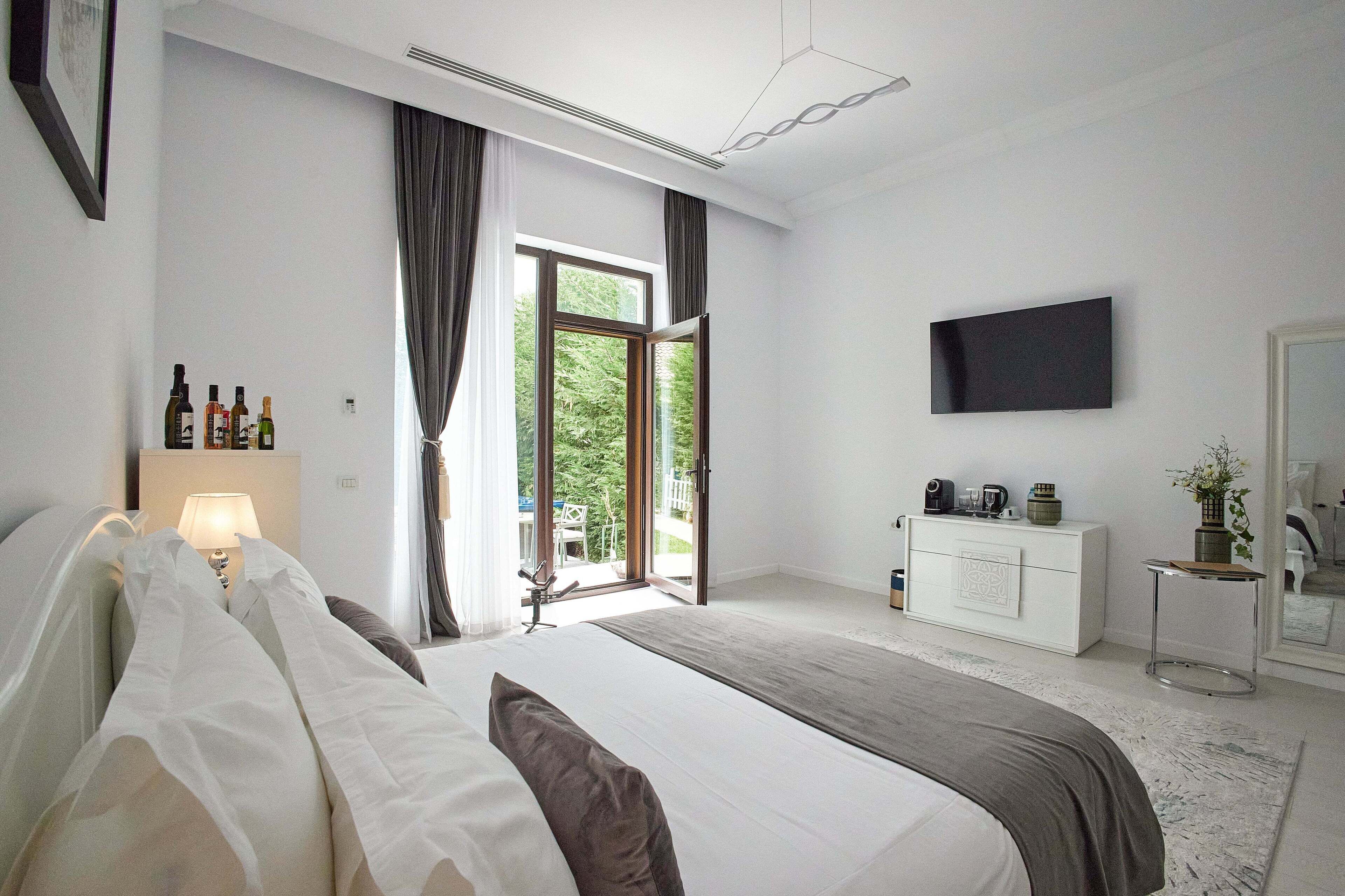 A modern bedroom with a large bed, a TV mounted on the wall, a dresser, and a window with curtains.