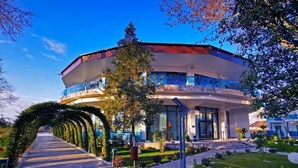 A modern building with a curved facade, a central entrance, and a landscaped pathway leading to it. - Lebada Luxury Resort & Spa (Crisan)