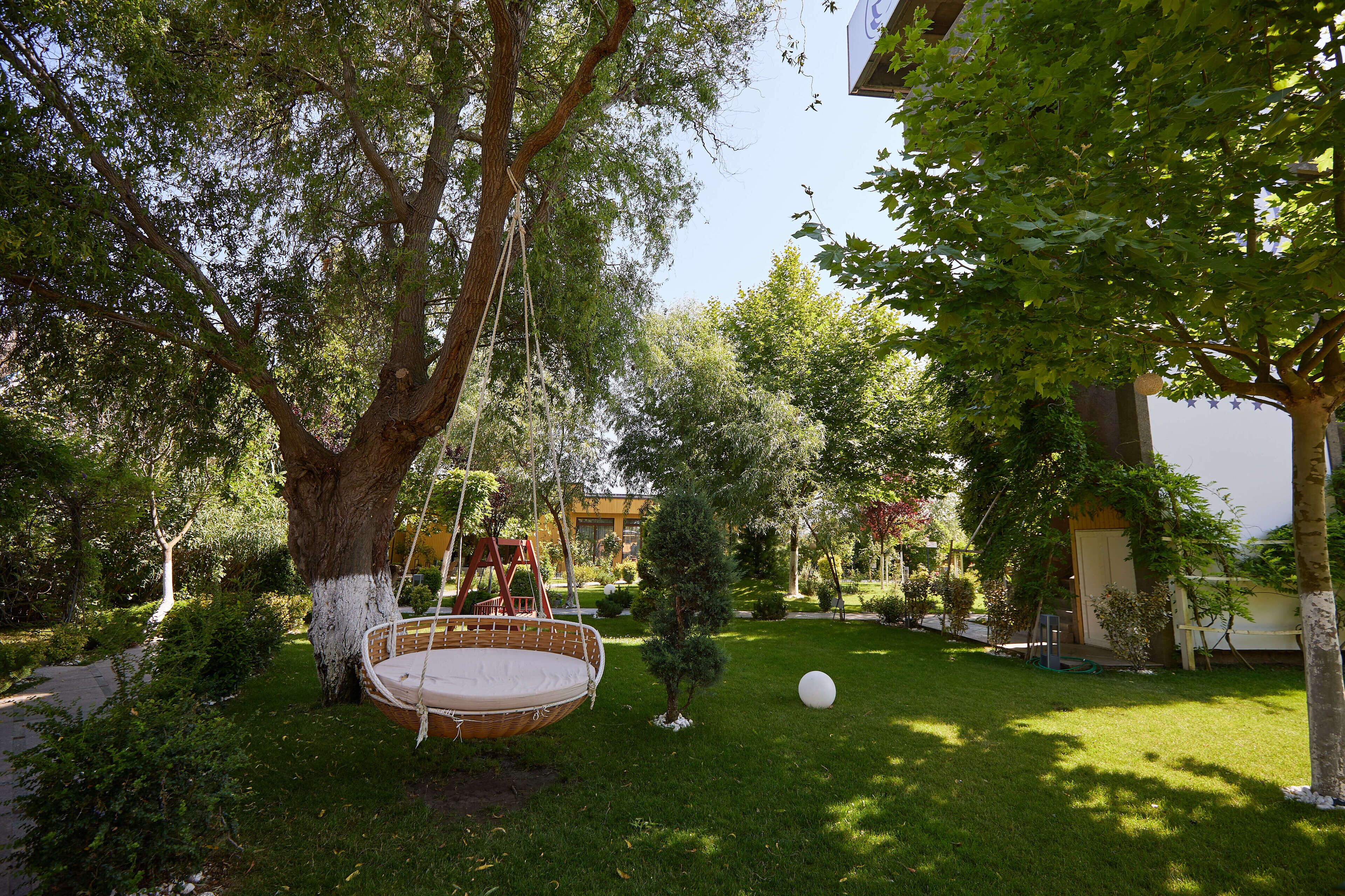 A garden with a swing chair, a small tree, and a white spherical object on the grass.