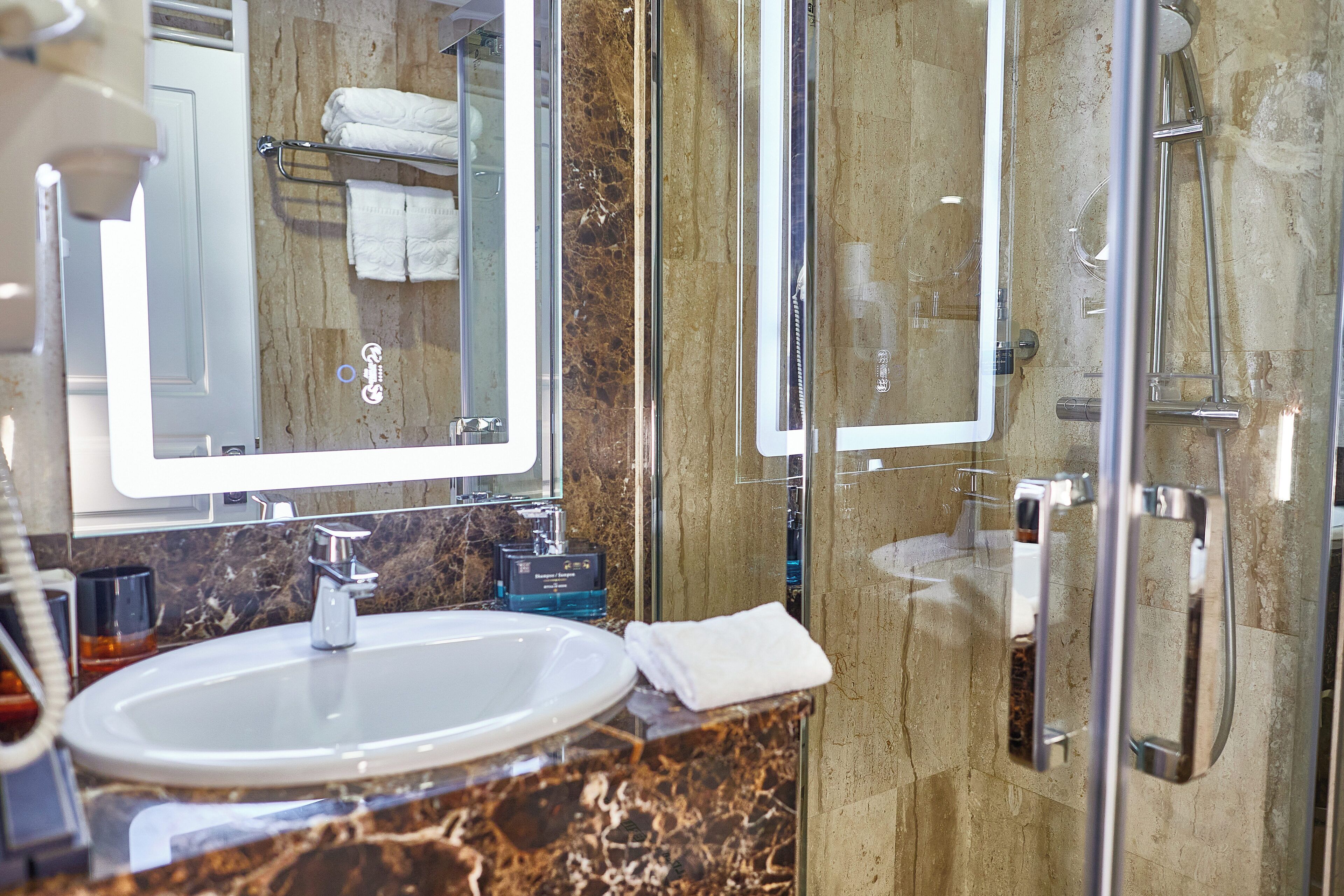Ein modernes Badezimmer mit Marmorplatte, einem weißen Waschbecken und einer Duschkabine aus Glas.