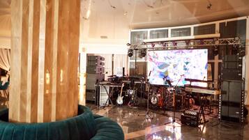 A spacious room with a stage setup for live music, including a keyboard, drums, and guitars.