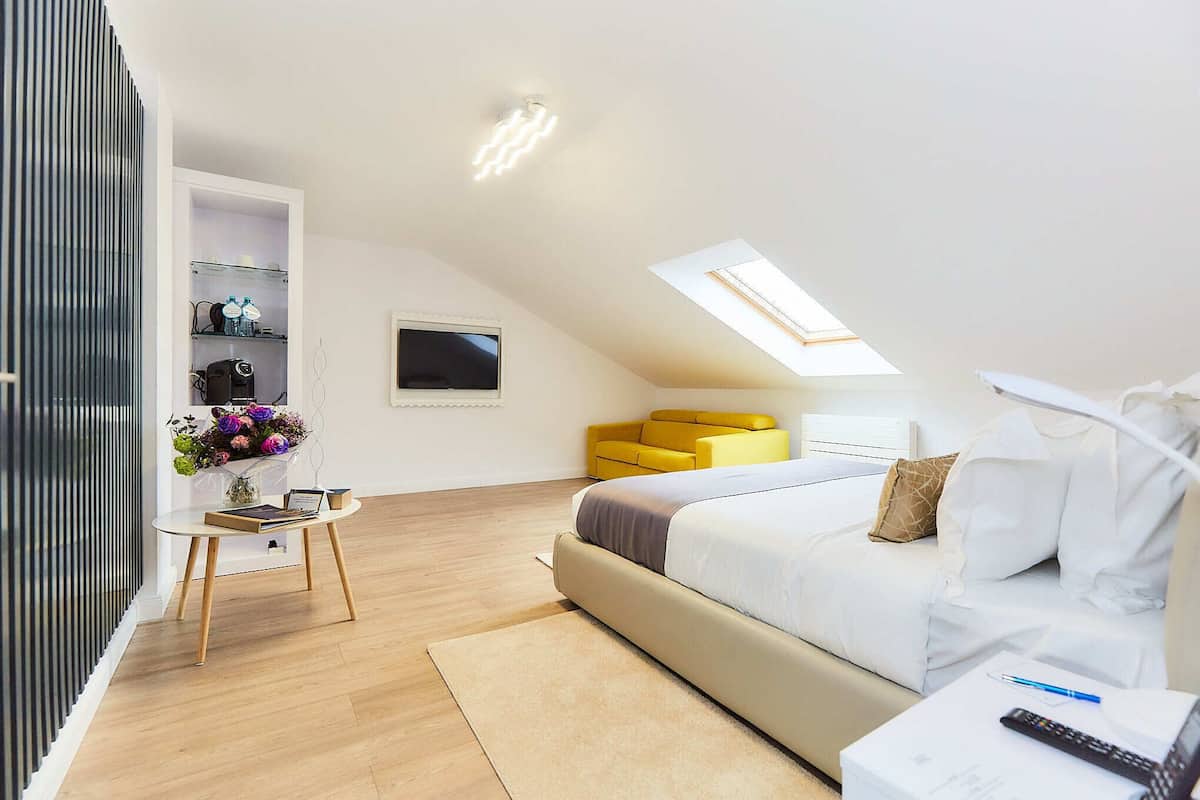 A modern bedroom with a bed, a yellow chair, a small table with a vase of flowers, and a skylight.