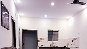 A modern kitchen with dark cabinets, a window, and a ceiling fan. - Roomshala 135 Paradise Villa Banglore (Devanahalli)