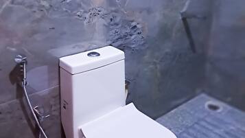 Un baño con inodoro blanco, ducha y pared de mármol.