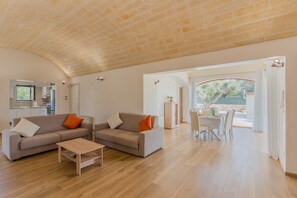 A spacious living area with a brick ceiling, a sofa set, a dining table, and a view through an open archway.