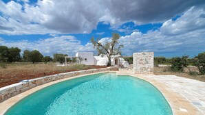 A swimming pool with a stone border, a white building, and a tree in the background. - Villa 'Trullo White Dream Con Piscina' with Private Pool, Wi-Fi and Air Conditioning (Ostuni)