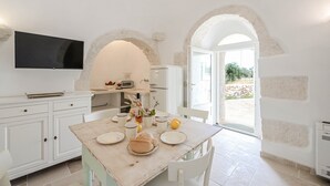 A dining area with a table set for two, a television mounted above, and a view of the outdoors through an arched doorway. - Villa 'Trullo White Dream Con Piscina' with Private Pool, Wi-Fi and Air Conditioning (Ostuni)